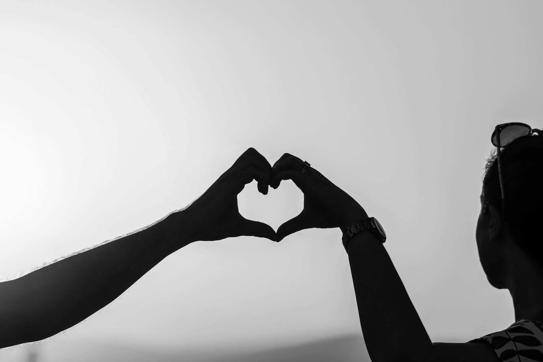 Black and white photo of a couple forming heart shape with hands, symbolizing love.