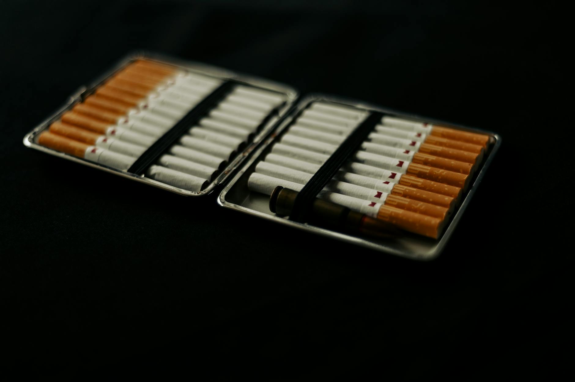 An open cigarette case filled with cigarettes, placed on a dark surface, conveying a mood of smoking and lifestyle.