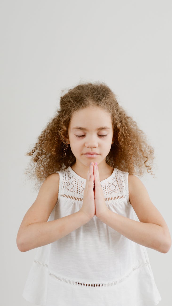 A young girl with curly hair meditating indoors, conveying peace and tranquility.